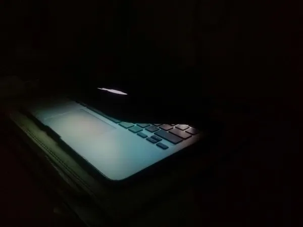 A laptop in a dark room with only the screen's light illuminating the surroundings.