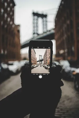 A person holding a telephone and taking a photo of a bridge in the background.